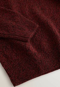 Dark red and black knit sweater folded to show textured cuff and hem with ribbed edges on a light background.