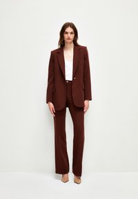 Bruin op maat gemaakt pak met een gestructureerde blazer en rechte broekspijpen. Draag een wit topje eronder, met een subtiele glans en schone lijnen.