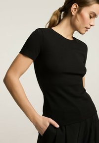 Czarny prążkowany t-shirt z krótkim rękawem, okrągłym dekoltem, dopasowany fason i gładka tekstura, z delikatnym połyskiem.