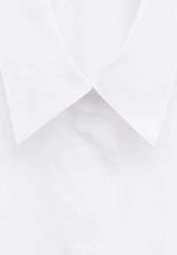 Nærbillede af en hvid skjortekrave med spidse ender og en synlig knap under.