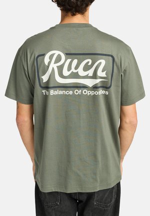 Olijfgroen katoenen T-shirt met korte mouwen. Witte tekst op de achterkant leest "Rucn" met daaronder "The Balance Of Opposites", omlijst door een rechthoek.