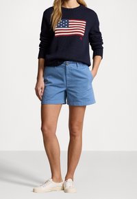 Mörkblå stickad tröja med amerikanskt flaggmönster, ljusblå bomullsshorts och vita sneakers. Tröjan har ribbade ärmslut och nederkant.