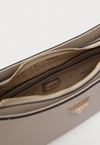 Beżowa syntetyczna torebka o fakturowanej powierzchni, z złotym zamkiem i logo „GUESS”. Wnętrze posiada wiele przegródek i gładką podszewkę.