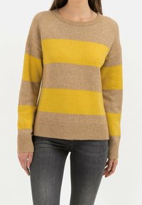 Striktrøje med brune og gule vandrette striber, rund hals og ribbede manchetter. Blød tekstur, afslappet pasform. Båret med mørke jeans.