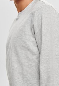 Maglia a maniche lunghe grigio chiaro con scollo rotondo e tessuto liscio, progettata con una vestibilità rilassata e cuciture minime.