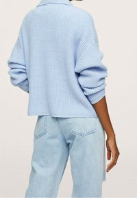 Cárdigan de punto azul claro con un corte relajado, que presenta hombros caídos y puños enrollados, combinado con jeans azul claro.