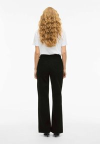 Crne široke hlače od čvrstog materijala, s visokim strukom i dva stražnja džepa, uparene s običnom bijelom majicom.