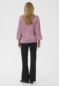 Suéter rosa brillante con mangas sueltas y dobladillo acanalado, combinado con pantalones negros acampanados y zapatos brillantes, visto desde la parte trasera.