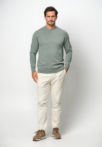 Maglione verde chiaro con maniche lunghe, abbinato a pantaloni color crema e sneaker in suede marrone. Design semplice e aderente.