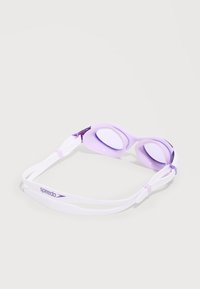 Λευκά και λιλά γυαλάκια κολύμβησης Speedo που ακουμπούν σε λευκή επιφάνεια, με ρυθμιζόμενους ιμάντες και σκουρόχρωμους φακούς.