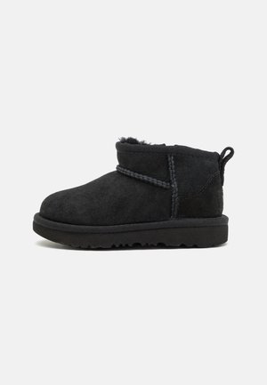 Bota de tornozelo em camurça preta com bico arredondado, detalhes nas costuras laterais e um interior com forro suave. Apresenta uma sola de borracha texturizada e uma alça na parte traseira.