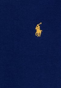 Námořnická modrá pletenina má malé žluté vyšívané logo polo hráče, s hladkým povrchem a rovnoměrným stehem po celé ploše.