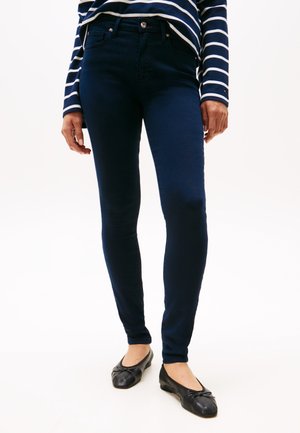 Marineblå skinny jeans med en glatt tekstur, fem-lommemodell og knappelukking, sammen med svarte ballettsko.