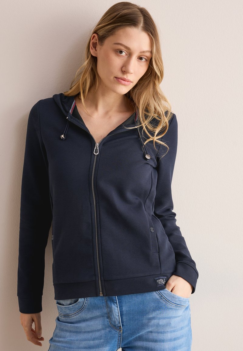 Sweat à zip marine fabriqué en tissu texturé, avec une capuche à cordon, des poches latérales et une broderie logo à l'ourlet.
