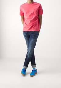 Rosa bomull t-shirt, blå denim jeans och blå mockaskor med röda detaljer. Ledig passform med uppvikta ärmar på jeansen.