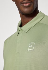 Lys grøn polo skjorte med teksturert stoff, med en hvit Nike-logo i rektangulært design og klassisk krage.