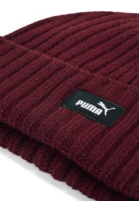 Bordeaux geribbelde gebreide muts met omgeslagen rand, voorzien van een zwart patchlabel met witte Puma-logo en tekst.