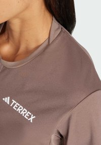 Terrex sportstrøje i lys brun med rund halsudskæring og korteærmer. Hvidt logo placeret på venstre side. Glat tekstur.