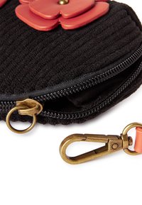 Tule negra con textura estriada, con tres apliques florales rojos, un cierre dorado y un clip de llavero de latón con un acento naranja.