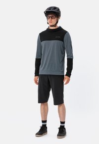 Abbigliamento sportivo maschile con una maglietta a maniche lunghe color turchese con dettagli neri, abbinata a pantaloni corti neri e scarpe nere. Include un casco da ciclismo.