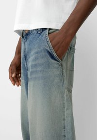 Light blue denim jeans featuring a relaxed fit, faded texture, and side pockets. Paired with a plain white t-shirt.