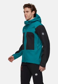 Blauwgroene en zwarte weersbestendige jas met ritszakken, een capuchon, rekbare stof en een logo-accent op de mouw.