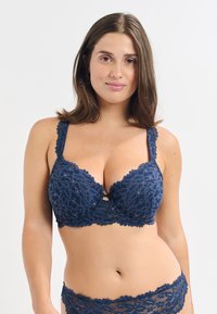 Reggiseno in pizzo blu navy con motivo floreale, bordi ondulati e spalline regolabili. Presenta un design a chiave centrale e un tessuto morbido e texture.