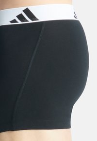 Svarta boxerkalsonger med ett vitt elastiskt midjeband som har en svart tre-strips logotyp. Slät textur och tajt design.