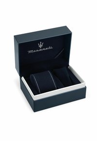 Scatola in pelle blu navy con logo Maserati argentato. Contiene due rotoli di tessuto scuro con cuciture bianche, che mostrano una consistenza morbida.