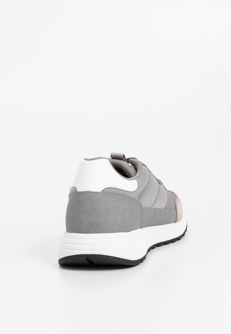 Grauer Sportschuh aus einer Kombination von Wildleder und Mesh-Materialien, mit einem weißen Fersenakzent, strukturierten Oberflächen und einer schwarzen Gummisohle.