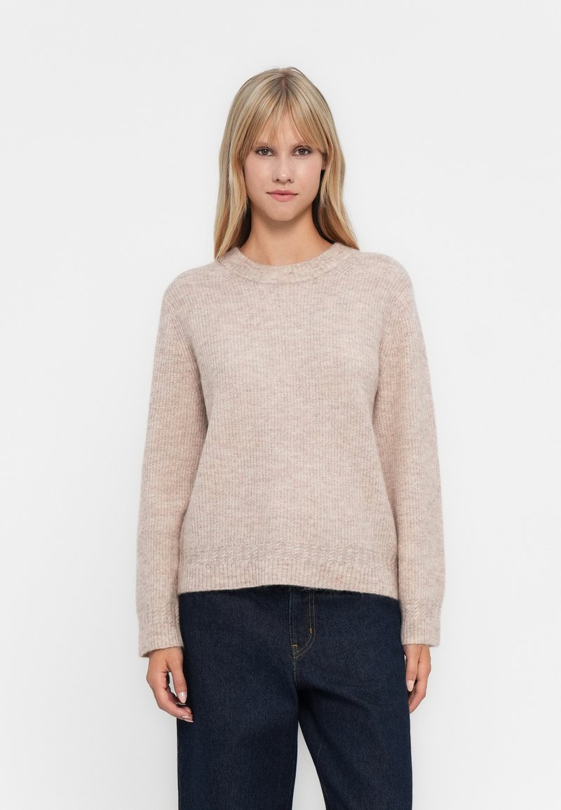 Ανοιχτό ροζ πλεχτό πουλόβερ με μακριά μανίκια, στρογγυλή λαιμόκοψη και χαλαρή εφαρμογή. Μαλακή υφή με ριμπ τελείωμα και μανσέτες, συνδυασμένο με σκούρα τζην.