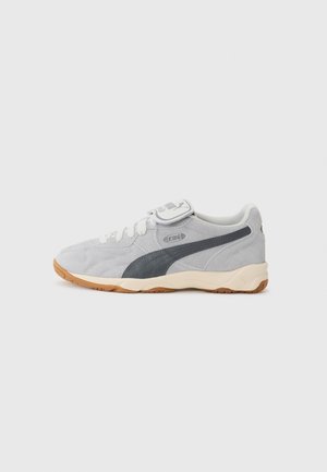 Baskets Puma King en daim gris clair avec lacets blancs, bande grise foncée sur le côté, semelle beige et semelle extérieure couleur gomme sur fond uni.