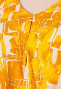 T-shirt à manches courtes en jaune et blanc, présentant un motif géométrique, en tissu de coton doux, avec une couture froncée au niveau de l'encolure.