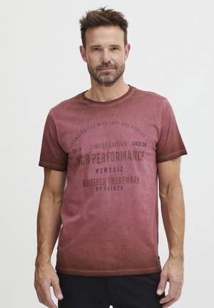 Tílko s krátkým rukávem v maroon barvě s gradientním designem. Obsahuje potištěný text v tmavě hnědé barvě, kulatý výstřih a volný střih.