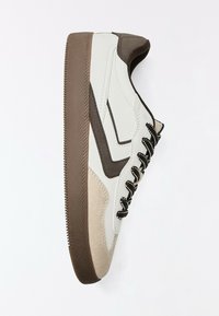 Baskets blanches avec des accents marron et beige, des lacets noirs et blancs, et une semelle marron texturée sur un fond blanc uni.