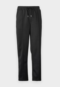 Svart joggebukser med snor i midjen, elastisk mansjett og glatt stoff med subtile detaljer på sidene. Ingen synlig maskinvare.