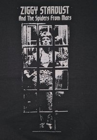 T-shirt nera con una grafica bianca di una figura dietro una griglia, con la scritta "ZIGGY STARDUST E I RAGNI DI MARTE."