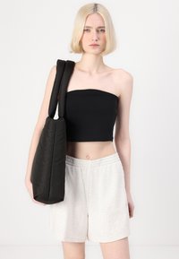 Svart avskuren strapless topp, ljusgrå shorts och en stor svart tote-väska. Släta texturer, minimal design och en monokrom färgskala.