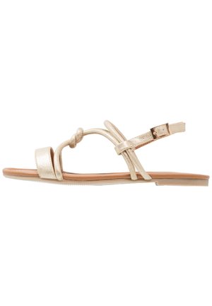 Guldmetallic flade sandaler med knotted detaljer, tynde stropper og en justerbar ankelrem. Flad sål, minimalistisk design.