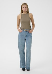 Barna bordázott ujjatlan felső világoskék egyenes szárú farmerrel és ezüst szegecses övvel, texturált felülettel és lapos cipővel.