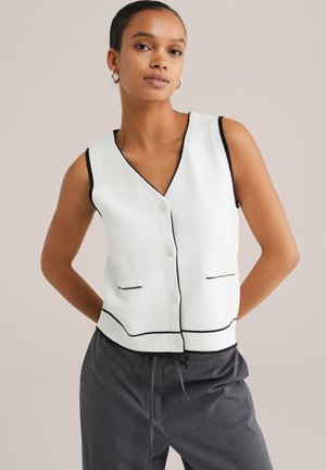 White sleeveless vest with black trim, featuring a V-neckline, five buttons, and two front pockets; smooth knit texture.