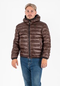 Bruine pufferjack met capuchon, met een glanzende afwerking, horizontale stiksels en een rits aan de voorkant. Ribgebreide manchetten en een klein logo-detail.