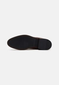 Suela de zapato de cuero marrón con una capa de goma negra texturizada. Presenta un borde suave y un delgado relieve con patrón a lo largo del perímetro.