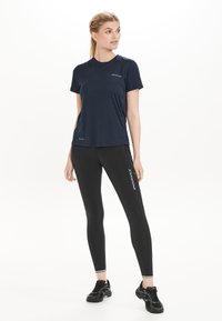 Navy urheilu t-paita lyhyillä hihoilla ja pyöreällä kaula-aukolla, yhdistettynä mustiin leggings-haalareihin, joissa on valkoista "ENDURANCE"-tekstiä; molemmat on valmistettu kosteutta siirtävästä kankaasta.