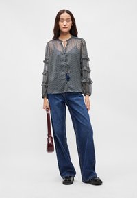 Μπλούζα με μακριά μανίκια, σε ναυτικό μπλε χρώμα και σχέδιο, με ζακάρ μανίκια, λεπτομέρεια κόμπου και κουμπιά μπροστά. Συνδυασμένη με παντελόνι σε φαρδιά γραμμή σε μπλε χρώμα και burgundy τσάντα.