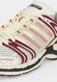 Λευκό και μαρονί παπούτσι Adidas adiStar με επάνω μέρος από δίχτυ και συνθετικές επικαλύψεις και κορδόνια με ροζ λεπτομέρειες πάνω στη δομημένη σόλα.