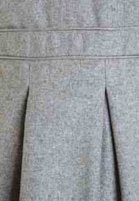 Szara wełniana spódnica o teksturowanej tkaninie, z plisowanym designem i dwoma poziomymi szwami w okolicy talii, zapewniającymi strukturę i kształt.