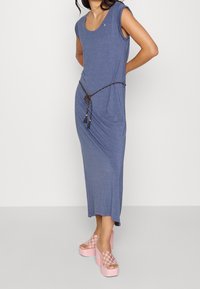 Niebieska sukienka do kolan z krótkimi rękawkami typu kaptur, ozdobiona plecionym brązowym paskiem z frędzlami. Do tego różowe sandały na platformie w kratkę.