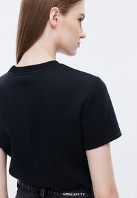 Camiseta negra de manga corta con cuello acanalado, textura suave y un corte relajado, combinada con pantalones cortos de mezclilla de cintura alta.