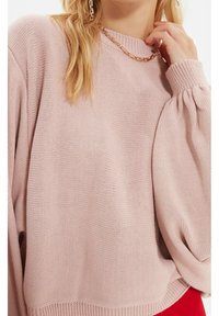 Pull en tricot rose clair avec un col haut, des manches longues bouffantes et un ourlet côtelé. Dispose d'un motif à tissage texturé et lâche.